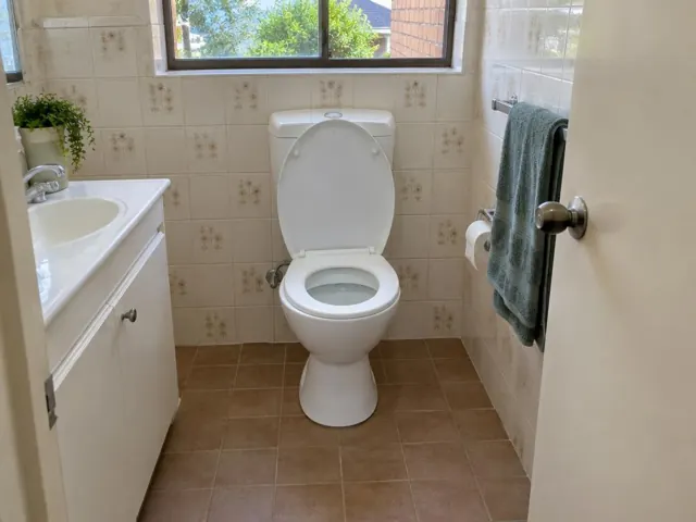 White toilet in a tiled bathroom with vanity, towel and window in Collaroy