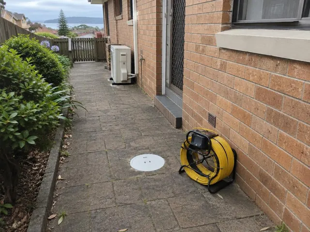 Capped drain inspection opening beside a coiled camera reel on a brick side path by a house in Cromer